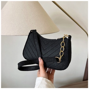 Detail of black felt underarm bag featuring V-shaped quilting and a gold chain strap