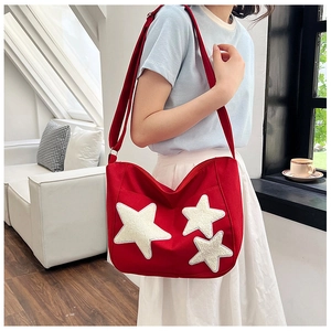Détail d'un sac bandoulière en toile rouge avec étoiles en peluche blanches sur un cabas