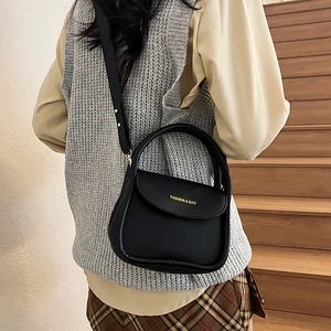 Sac à main bandoulière noir mat avec lettrage doré porté par un mannequin dans un décor