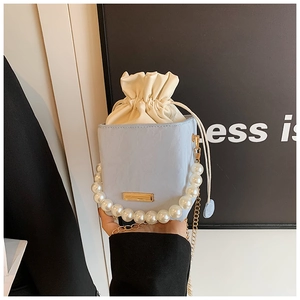 Close-up of light blue drawstring bucket bag with pearl handle and gold chain strap