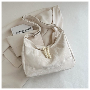 Detail of cream-colored shoulder bag with textured pleats and woven zipper charm