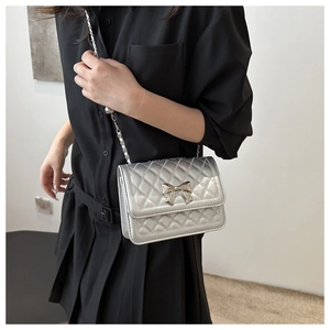 Close-up of silver quilted crossbody bag with metallic bow detail and chain strap