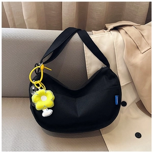 Détail du sac hobo en toile noire avec breloque fleur jaune sur un canapé texturé
