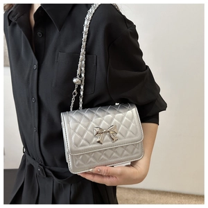 Detail of silver quilted crossbody bag featuring metal bow buckle and chain strap