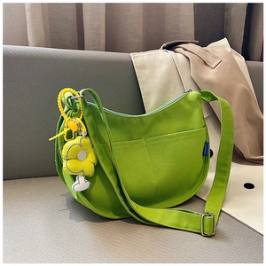 Détail du sac croissant en toile verte avec pendentif fleur jaune sur canapé