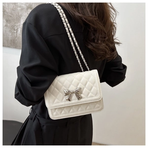Close-up of white quilted crossbody bag with silver bow detail and chain strap on model