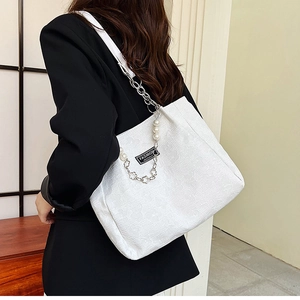 Détail d'un sac cabas en jacquard blanc avec chaîne argentée et breloque fleurie en perle