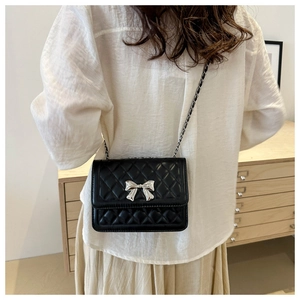 Detail of black quilted crossbody bag with silver bow clasp and metal chain strap