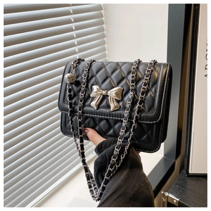 Close-up of black quilted shoulder bag featuring silver bow buckle and chain strap detail