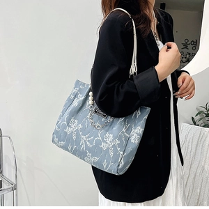 Détail du cabas bleu clair avec imprimé fleuri, breloque perle et étiquette en cuir