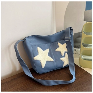 Détail du sac bandoulière en toile bleue avec étoiles en peluche sur bois sombre