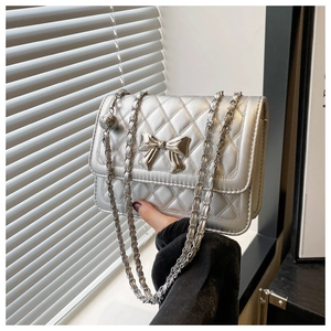 Detail of silver quilted faux leather crossbody bag with a metal bow buckle and chain strap