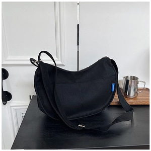 Détail du sac croissant noir avec étiquette tissée bleue et boucle en métal argenté