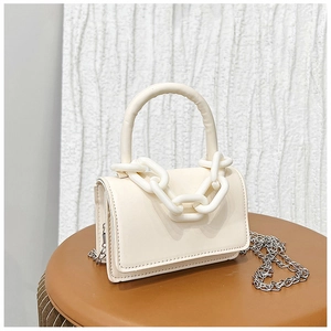 Détail d'un mini sac carré beige avec chaîne en résine et bandoulière sur un tabouret