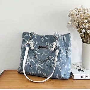 Détail du sac cabas en jacquard bleu avec chaîne de perles sur une table en bois