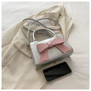 Detail of silver crossbody bag featuring a pink bow on a beige blazer setting