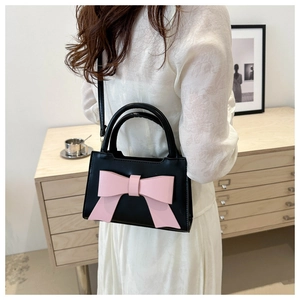 Close-up of stylish black crossbody bag featuring a large pink bow decoration on a model