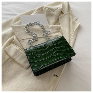 Detail of dark green crocodile texture on a small crossbody bag with silver chain