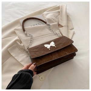 Detail of a brown pleated leather shoulder bag featuring a white butterfly ornament