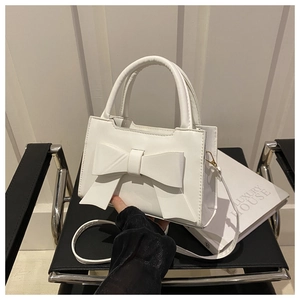 Detailed close-up of a white bow crossbody handbag on a black chair with a luxury prop book