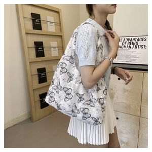 Detail of white tote bag featuring intricate black butterfly patterns and textured fabric