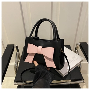 Detail view of black leather crossbody bag with a large pink bow on a chair