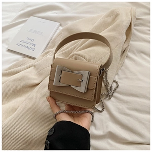 Detailed macro view of the silver bow metal clasp and leather texture on a beige square bag
