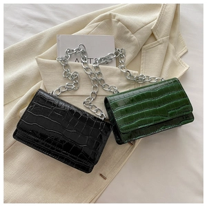 Detail of glossy crocodile pattern crossbody bags in black and green with silver chain