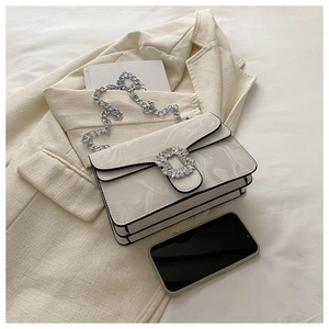 Detail shot of elegant cream-colored marble texture handbag with rhinestone buckle on suit