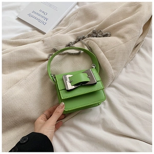 Detail of a grass green mini crossbody bag with silver buckle on a soft cream fabric