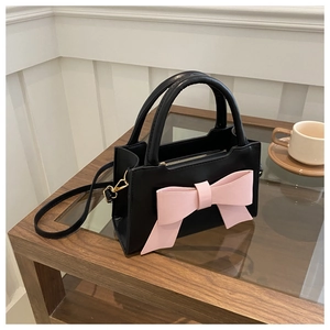 Detail of a chic matte black leather handbag with a large pink bow and gold hooks