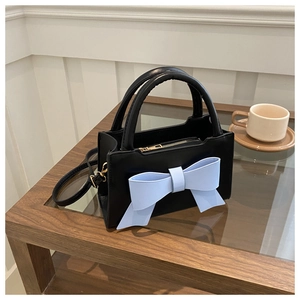 Close-up of black crossbody bag with blue bow on wooden table with coffee cup