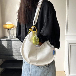 Sac hobo blanc en toile avec pendentif fleur jaune porté à l'épaule de façon décontractée