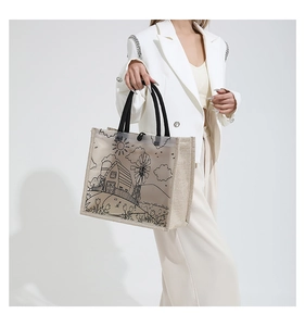 Close-up of beige linen tote bag featuring pastoral line art and woven black handles