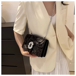 Detail of black glossy chain bag with wave texture and crystal buckle on beige blazer