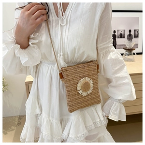 Detail of hand-woven straw crossbody bag featuring a white daisy decoration for summer