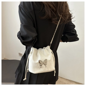 Close-up of a white drawstring bucket bag with silver butterfly and chain strap
