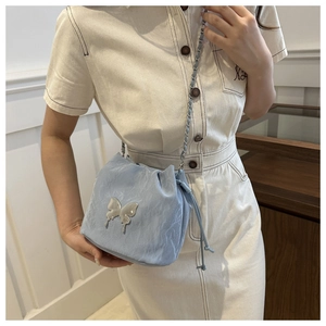 Detail of light blue drawstring bucket bag with silver butterfly and woven chain strap