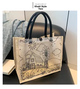 Detail of khaki tote bag with farm landscape print and black woven handle on leather chair