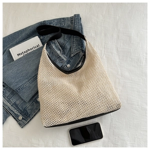 Détail d'un sac cabas tissé ajouré avec des anses noires sur une mise à plat décontractée