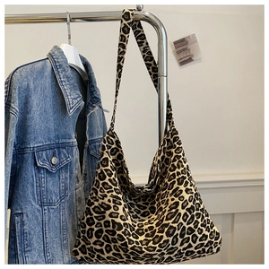 Detail of a large leopard print tote bag hanging next to a denim jacket on a hanger
