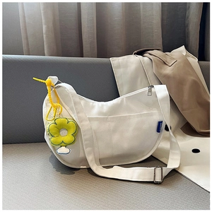 Détail d'un sac demi-lune en toile blanche avec étiquette bleue et breloque fleur jaune