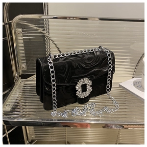 Detail of black glossy chain bag with rhinestone square buckle on acrylic shelf
