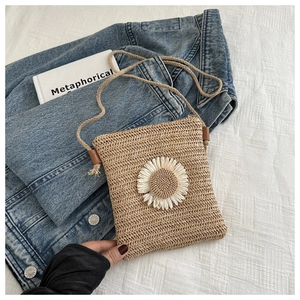Detailed view of woven straw crossbody bag with white daisy decor on fabric background