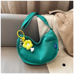 Détail du sac croissant en toile verte avec pendentif fleur de soleil sur canapé