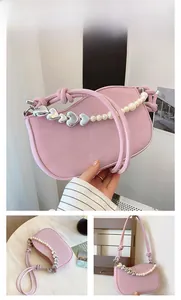 Detail of pink leather handbag featuring silver heart buckle and white pearl chain strap