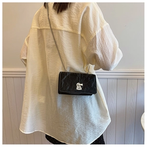 Close-up of a black textured crossbody bag with silver keyhole lock and chain strap