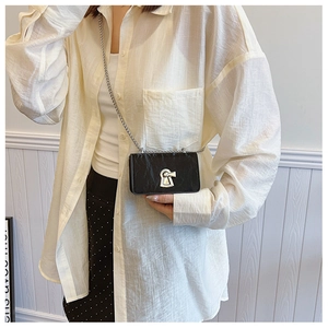 Model wearing a black mini crossbody bag with a large silver keyhole lock and chain strap