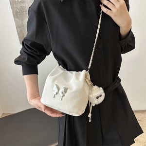 White bucket bag with silver butterfly charm and plush pompom, worn with a black dress
