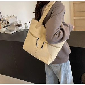 Close-up of beige canvas tote bag featuring parallel front zippers in a cafe setting